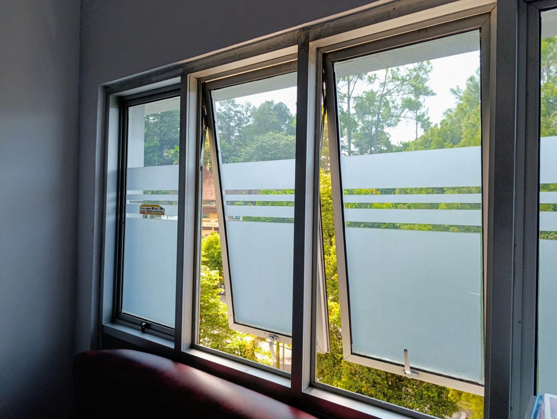 Modern glass windows with frosted privacy patterns, offering a serene view of lush green trees and a sunny outdoor landscape. Ideal for office or home design inspiration